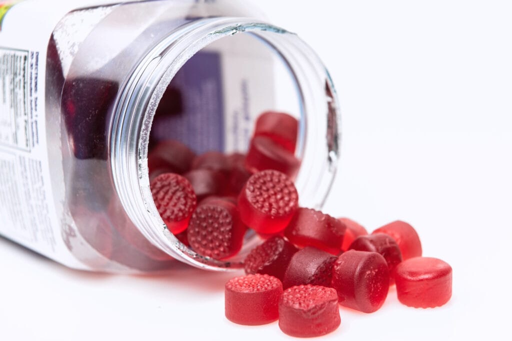 Red functional gummies spilling from a clear jar onto a white surface