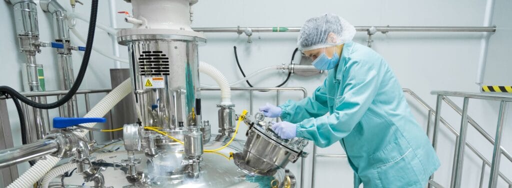 Operator in cleanroom clothing working with stainless-steel manufacturing equipment