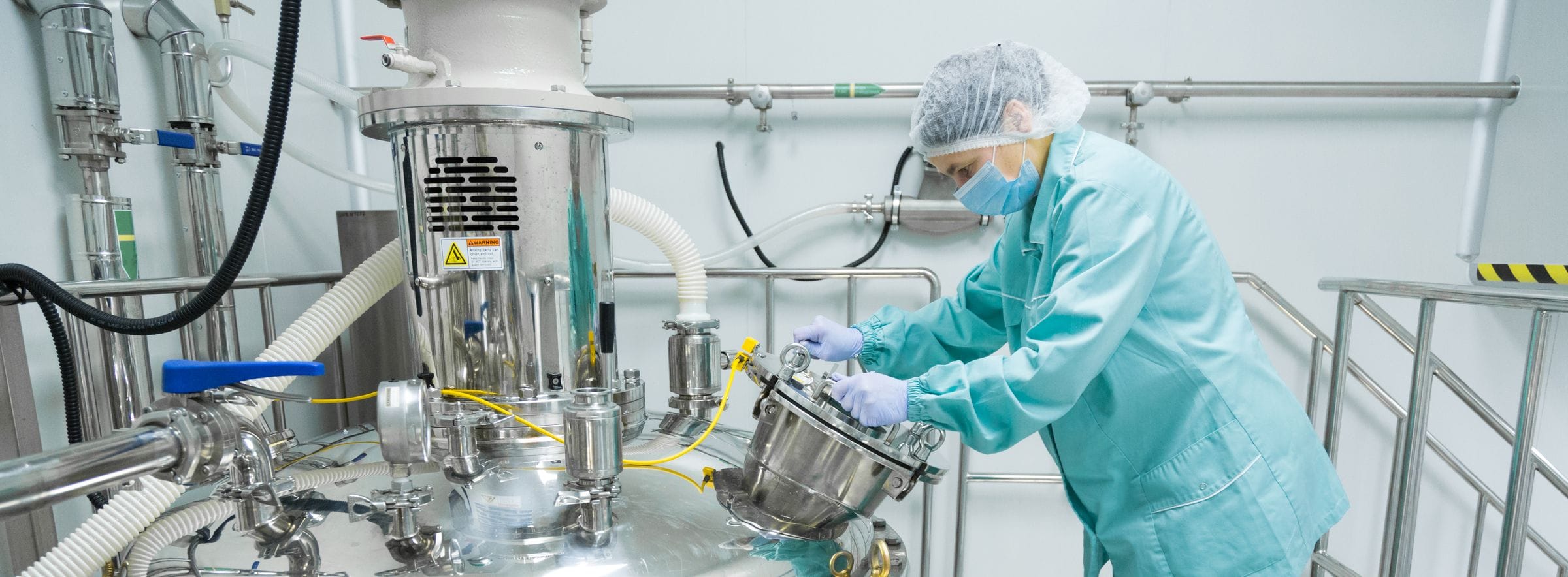 Operator in cleanroom clothing working with stainless-steel manufacturing equipment