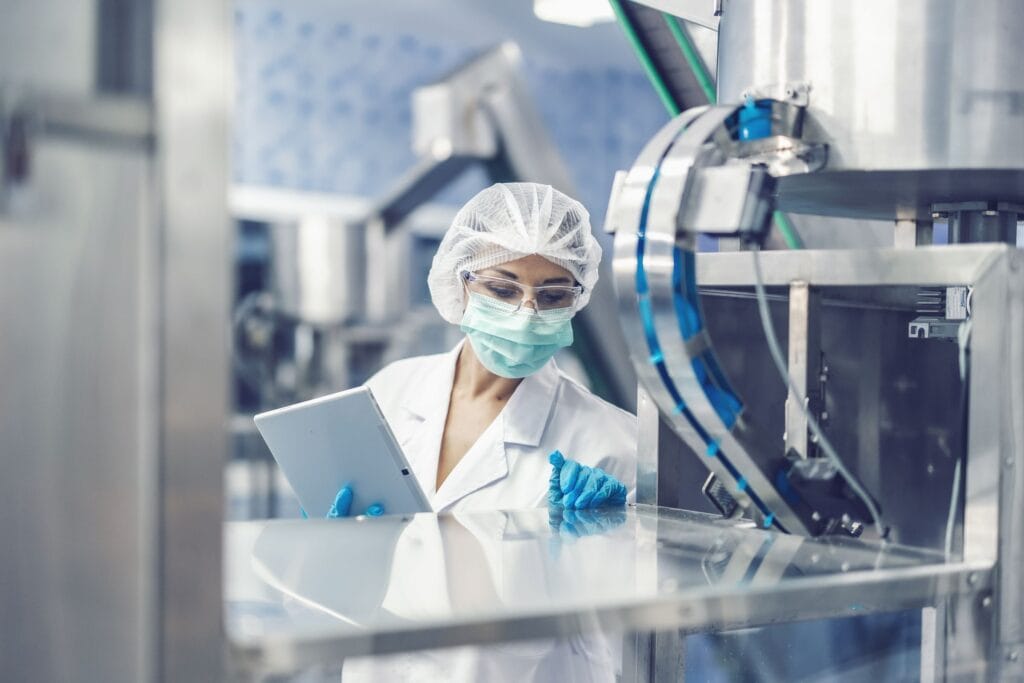 Technician in cleanroom clothing checking data beside production equipment